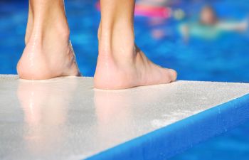 man's feet at edge of diving board before jumping into swimming pool