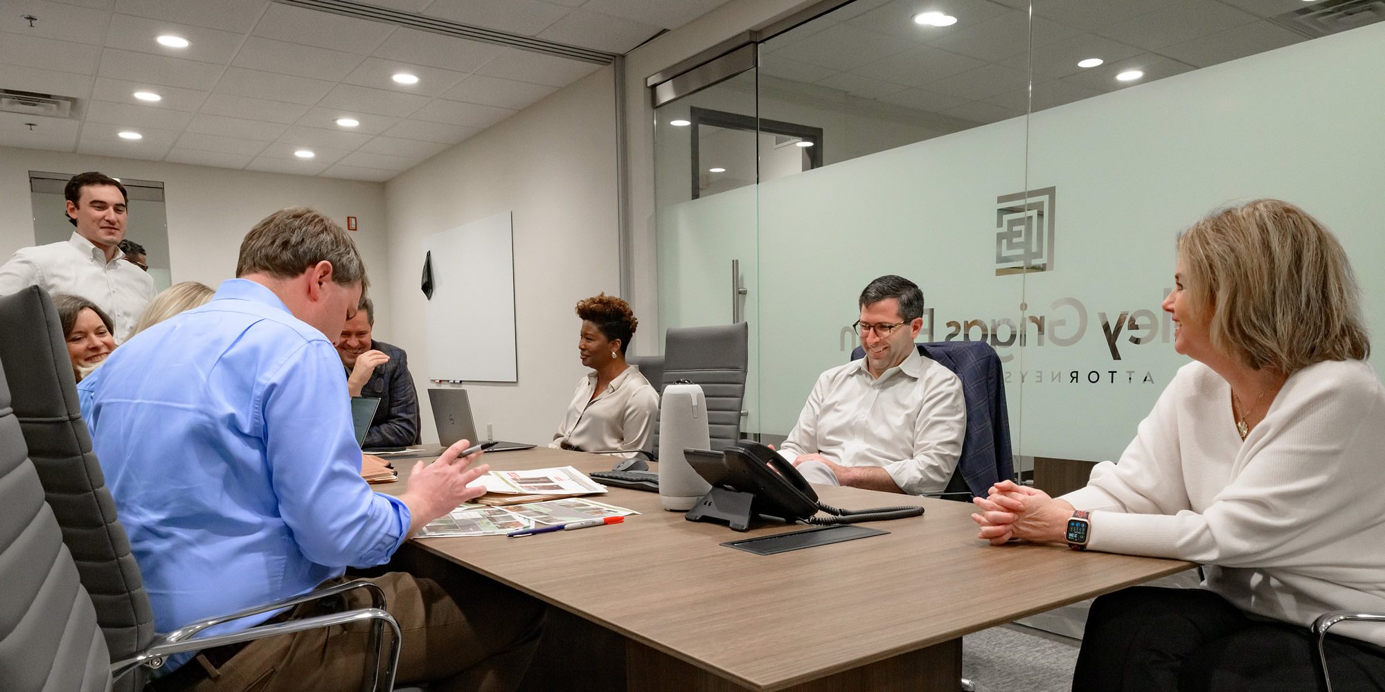 Business meeting in progress with a team of professionals collaborating around a conference table in a glass-walled office.